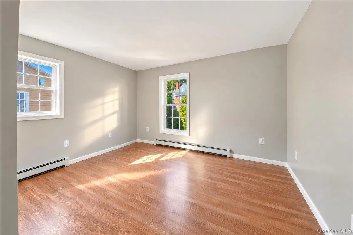 Spacious room featuring wood-finish flooring, light gray wall paint, and two double-hung windows with white trim Spacious room featuring wood-finish flooring, light gray wall paint, and two double-hung windows with white trim