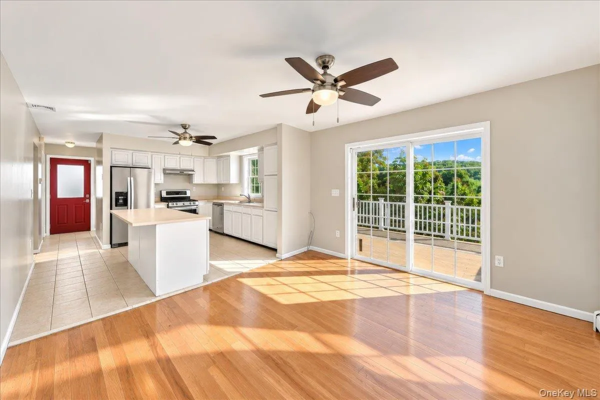 Hardwood-finish flooring and tile flooring, white kitchen cabinetry, stainless steel appliances, and a sliding glass door leading to a deck Hardwood-finish flooring and tile flooring, white kitchen cabinetry, stainless steel appliances, and a sliding glass door leading to a deck
