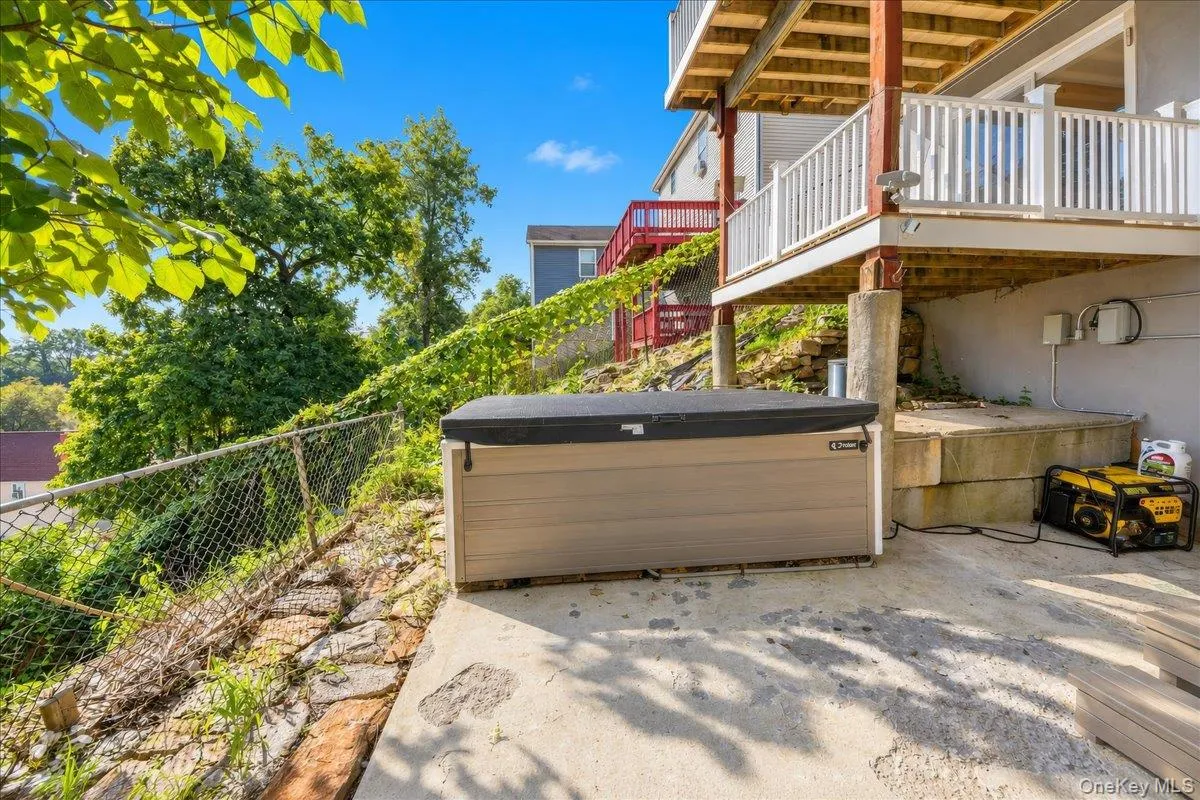 Tiered concrete patio featuring a hot tub, concrete retaining wall, and elevated deck with white balusters Tiered concrete patio featuring a hot tub, concrete retaining wall, and elevated deck with white balusters