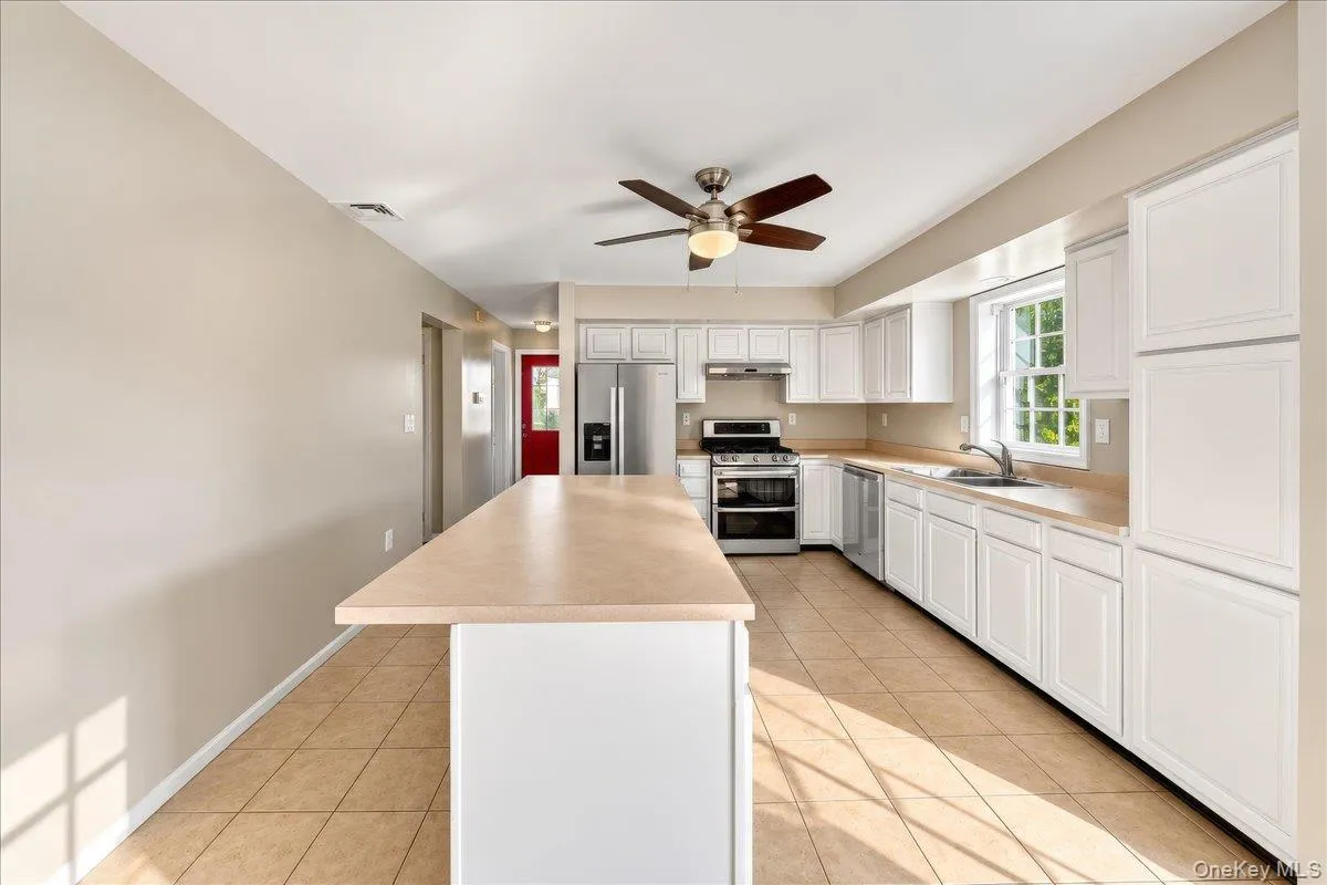 Kitchen featuring a central island with a breakfast bar, white cabinetry, a stainless steel refrigerator, a stainless steel range, and tile flooring Kitchen featuring a central island with a breakfast bar, white cabinetry, a stainless steel refrigerator, a stainless steel range, and tile flooring