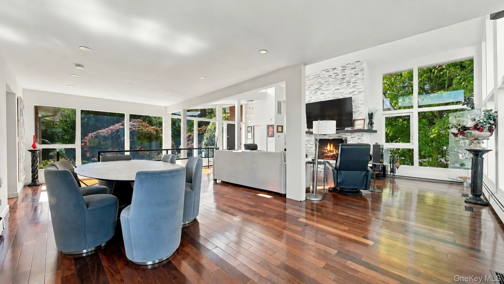 Open-concept interior featuring hardwood flooring, floor-to-ceiling windows, recessed lighting, and a floor-to-ceiling stone-veneer fireplace Open-concept interior featuring hardwood flooring, floor-to-ceiling windows, recessed lighting, and a floor-to-ceiling stone-veneer fireplace