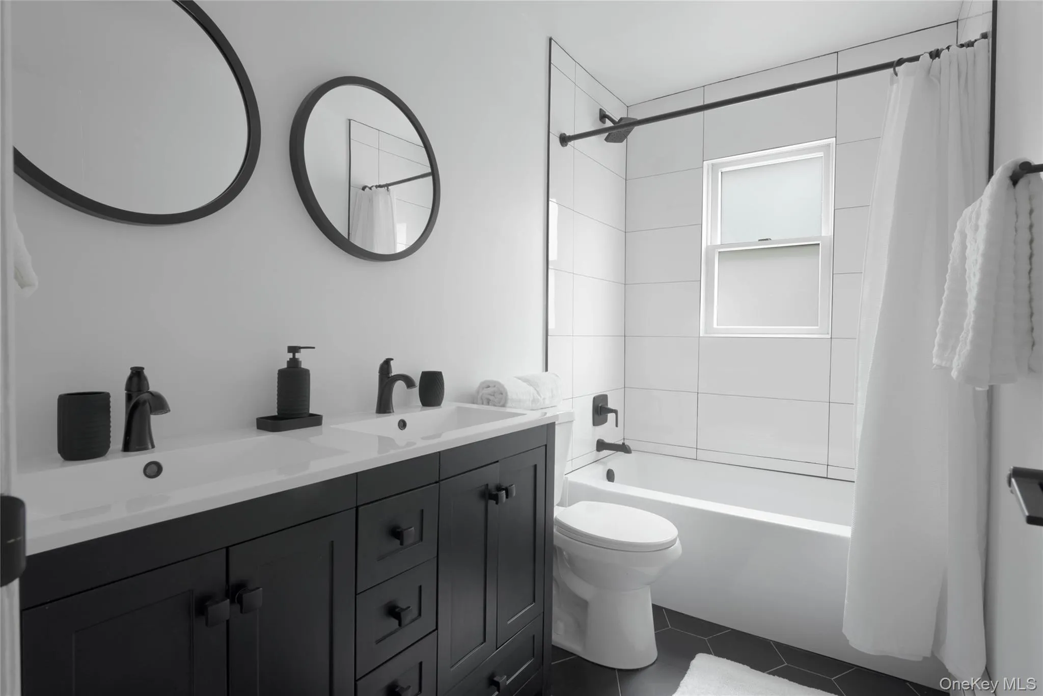 Full bathroom with double vanity, shower / bath combo with shower curtain, and dark tile patterned flooring Full bathroom with double vanity, shower / bath combo with shower curtain, and dark tile patterned flooring