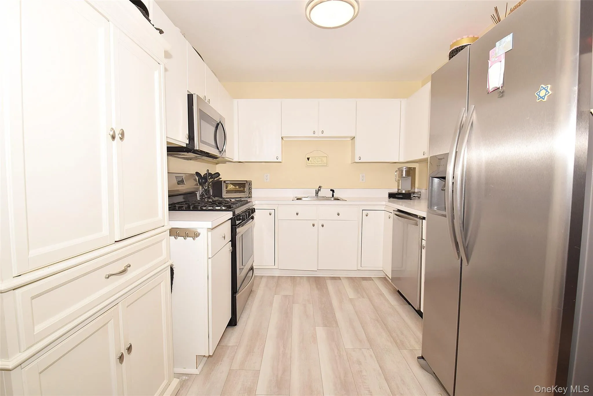 Kitchen featuring a sink, light countertops, light wood-style flooring, and appliances with stainless steel finishes Kitchen featuring a sink, light countertops, light wood-style flooring, and appliances with stainless steel finishes