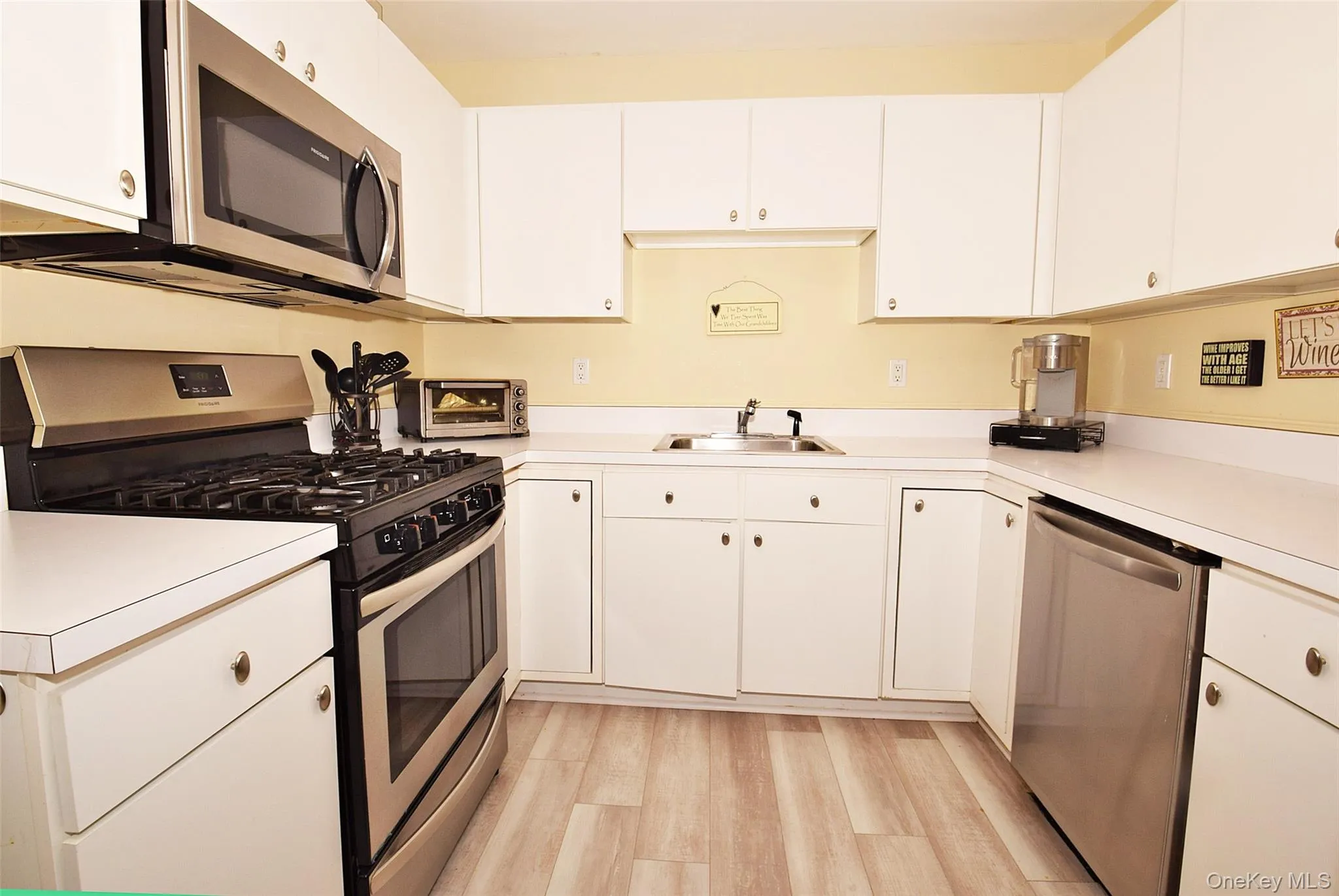 Kitchen with light countertops, a sink, light wood-type flooring, stainless steel appliances, and white cabinets Kitchen with light countertops, a sink, light wood-type flooring, stainless steel appliances, and white cabinets