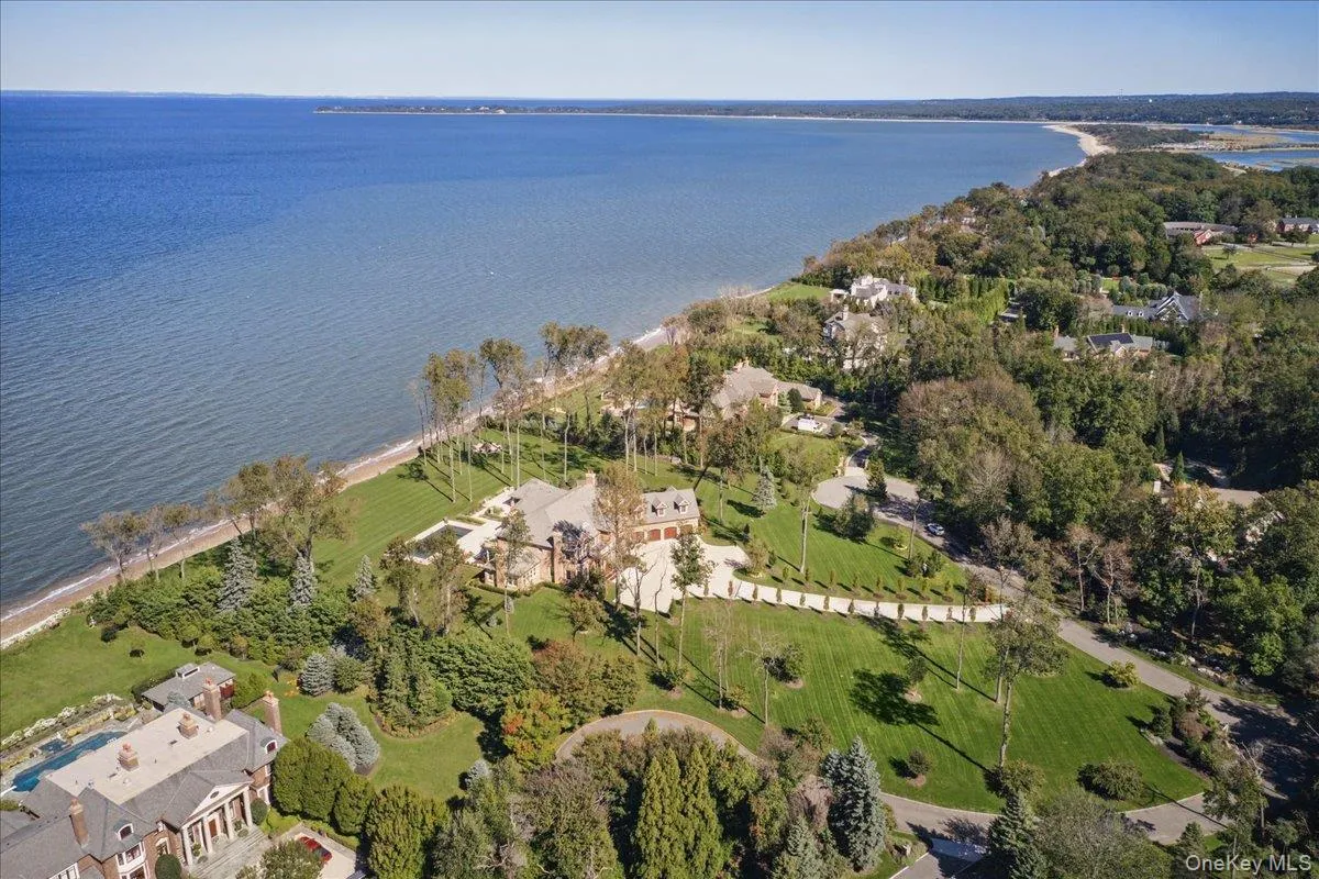 Expansive waterfront property featuring a large residence with a multi-gabled roofline, extensive manicured lawns, mature trees, and a swimming pool Expansive waterfront property featuring a large residence with a multi-gabled roofline, extensive manicured lawns, mature trees, and a swimming pool
