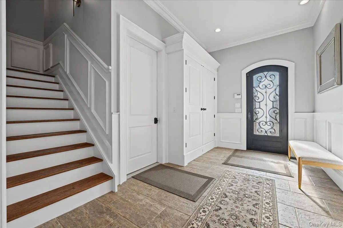 Entryway featuring tile flooring, wainscoting, an ornate arched entry door, a built-in storage cabinet, and a staircase with wood-finish treads Entryway featuring tile flooring, wainscoting, an ornate arched entry door, a built-in storage cabinet, and a staircase with wood-finish treads