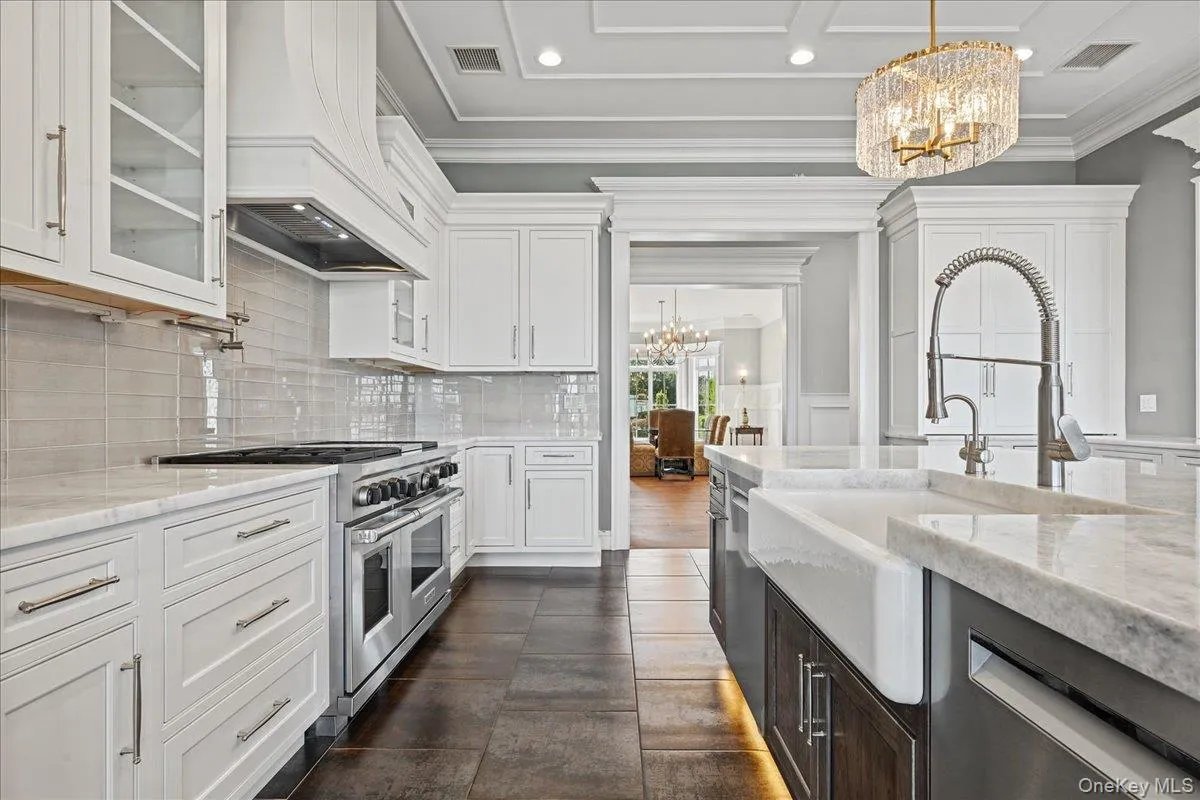 White cabinetry with glass-front uppers, stainless steel range, light-toned subway tile backsplash, and a farmhouse sink with a gooseneck faucet White cabinetry with glass-front uppers, stainless steel range, light-toned subway tile backsplash, and a farmhouse sink with a gooseneck faucet