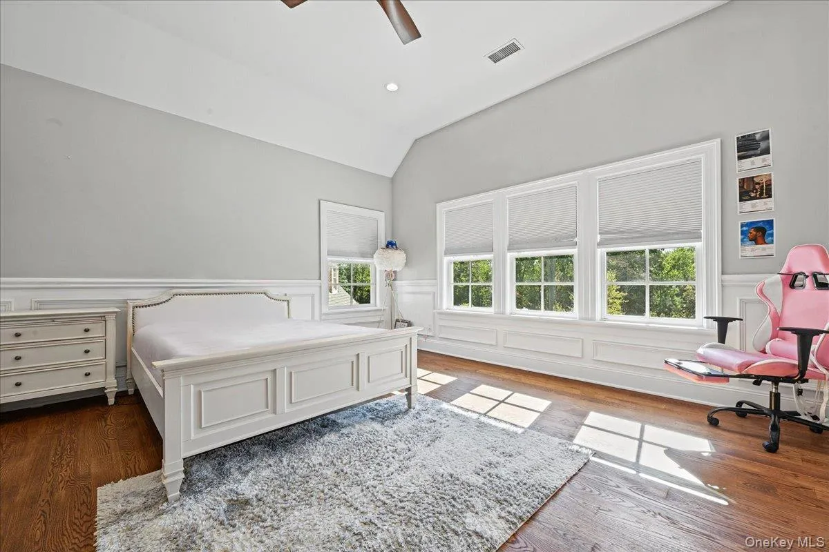 Vaulted ceiling with recessed lighting, wood-finish flooring, white paneled wainscoting, and large windows with cellular shades Vaulted ceiling with recessed lighting, wood-finish flooring, white paneled wainscoting, and large windows with cellular shades
