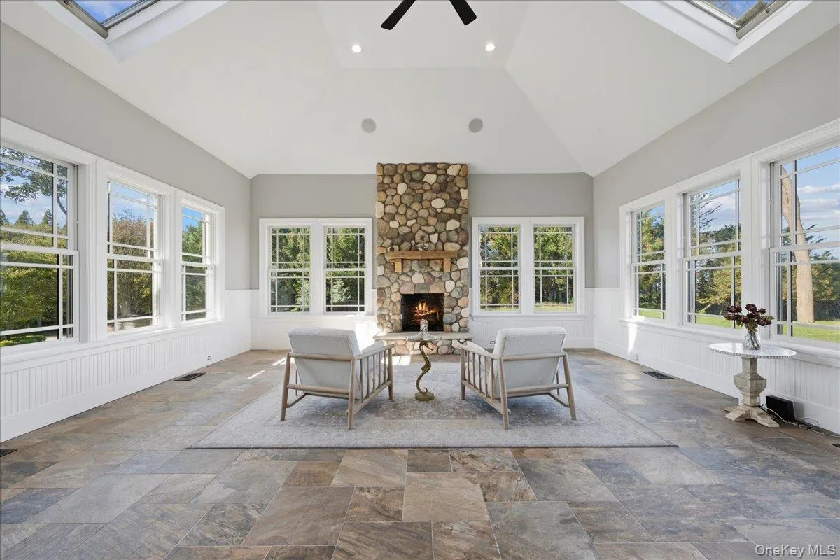 Vaulted ceiling with skylights, stone fireplace with wood mantel, tile flooring, and multiple windows with white trim Vaulted ceiling with skylights, stone fireplace with wood mantel, tile flooring, and multiple windows with white trim