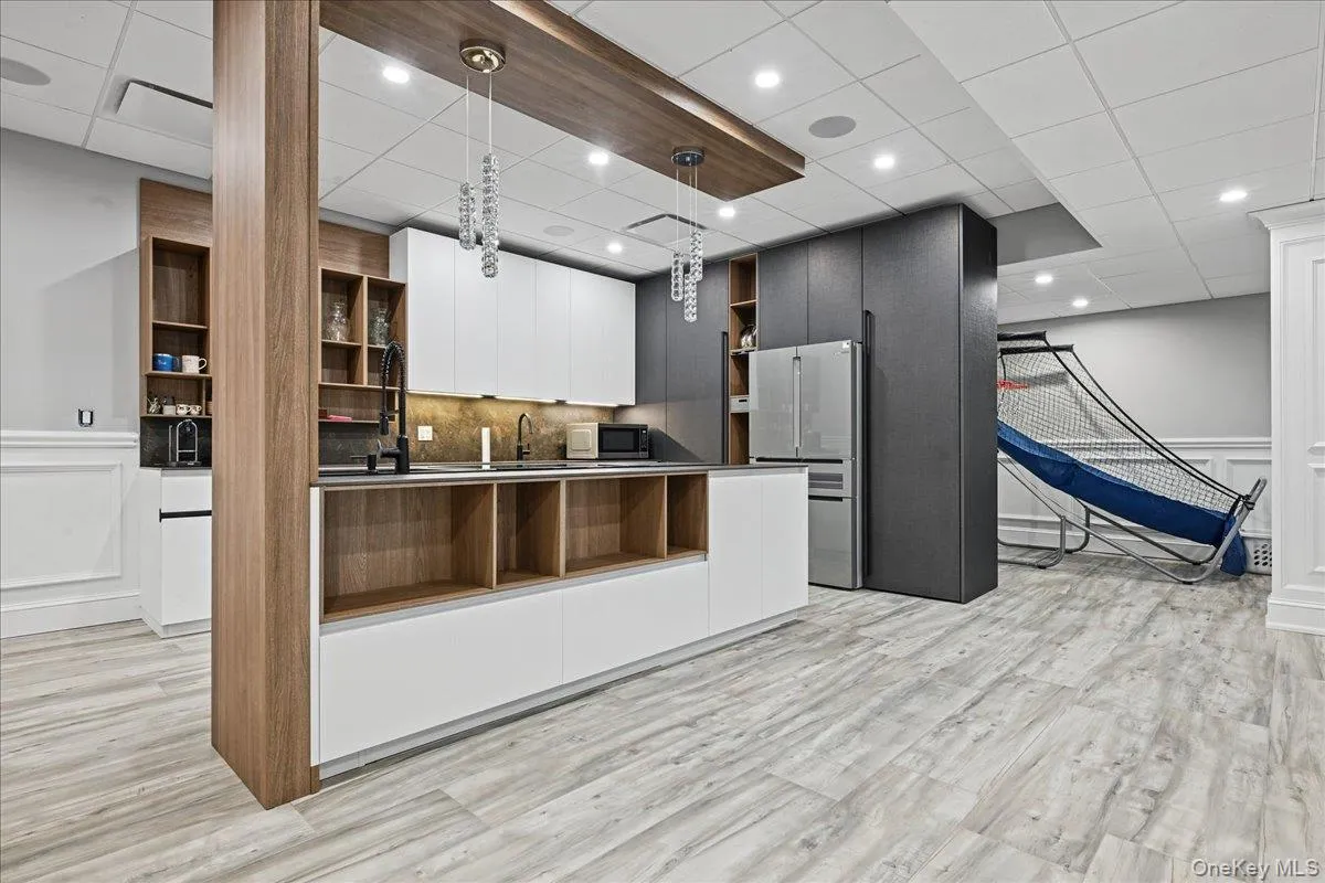 Modern kitchen area featuring light wood-finish flooring, white and charcoal cabinetry, built-in shelving, stainless steel appliances, and recessed lighting Modern kitchen area featuring light wood-finish flooring, white and charcoal cabinetry, built-in shelving, stainless steel appliances, and recessed lighting