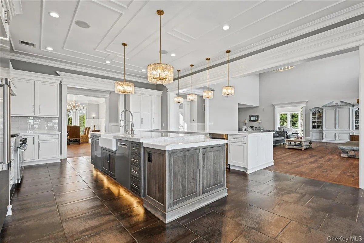 Gourmet kitchen featuring a large central island with farmhouse sink, decorative pendant lighting, white shaker cabinetry, and stone tile flooring Gourmet kitchen featuring a large central island with farmhouse sink, decorative pendant lighting, white shaker cabinetry, and stone tile flooring