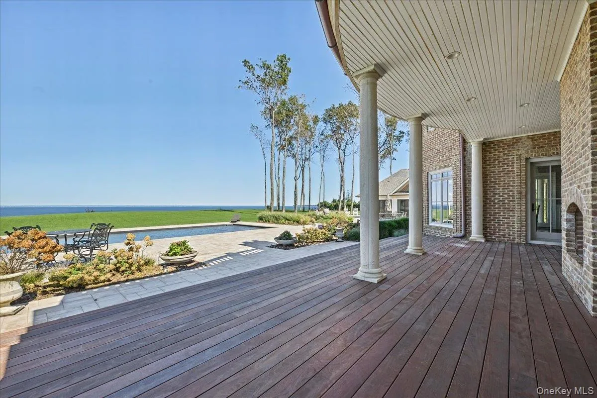 Expansive outdoor deck with dark wood-finish flooring, brick exterior, and white columns Expansive outdoor deck with dark wood-finish flooring, brick exterior, and white columns