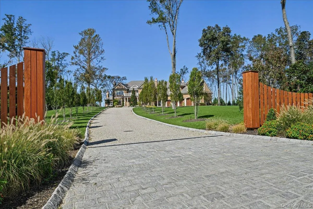 Paved driveway leading to a stone and brick exterior residence with a columned portico, surrounded by mature trees and manicured lawns Paved driveway leading to a stone and brick exterior residence with a columned portico, surrounded by mature trees and manicured lawns