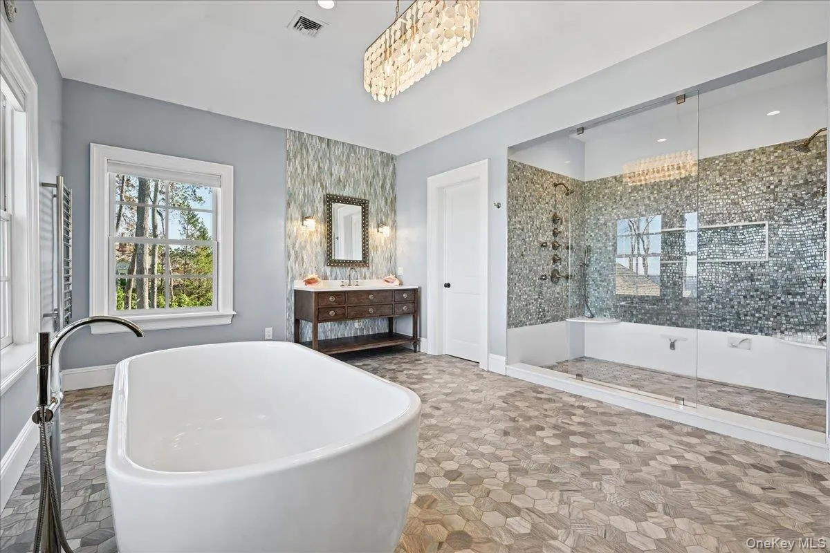 Freestanding soaking tub, walk-in shower with glass enclosure, wood-finish vanity with dual sinks, mosaic tile accent wall, and hexagonal floor tiling Freestanding soaking tub, walk-in shower with glass enclosure, wood-finish vanity with dual sinks, mosaic tile accent wall, and hexagonal floor tiling