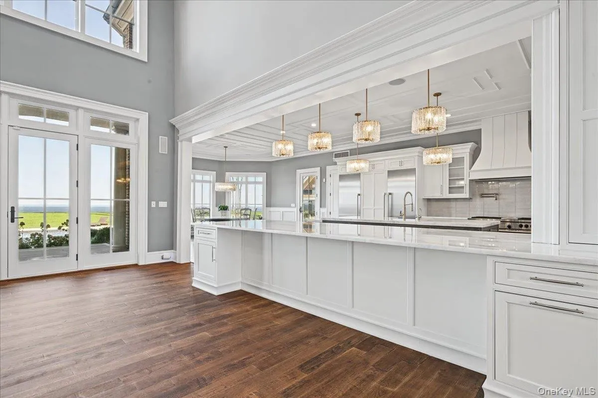 Spacious open-concept kitchen with wood-finish flooring, white cabinetry, a large kitchen island, and multiple pendant lights Spacious open-concept kitchen with wood-finish flooring, white cabinetry, a large kitchen island, and multiple pendant lights