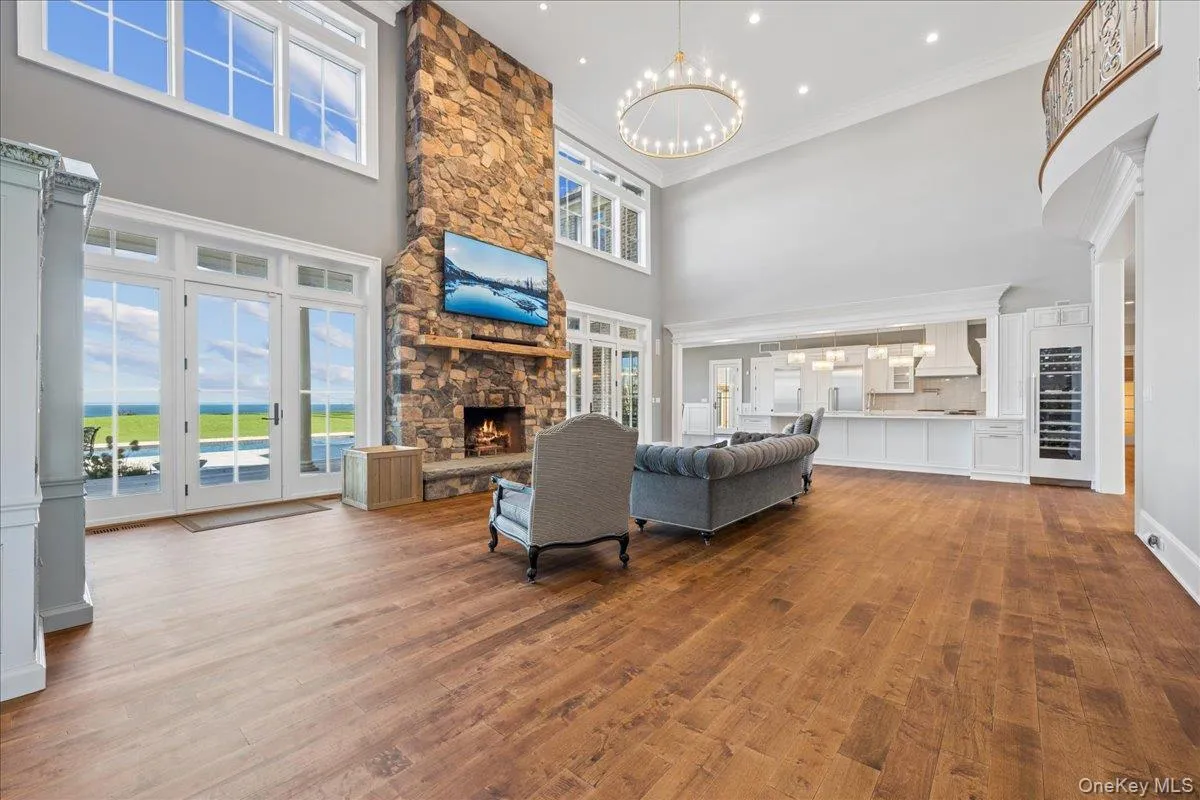 Two-story stone fireplace, wood-finish flooring, white double doors, upper transom windows, and a built-in wine refrigerator Two-story stone fireplace, wood-finish flooring, white double doors, upper transom windows, and a built-in wine refrigerator