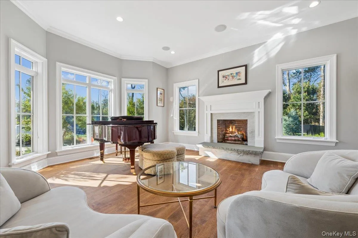 Wood-finish flooring, recessed lighting, crown molding, a built-in fireplace with a stone hearth, and multiple windows with white trim Wood-finish flooring, recessed lighting, crown molding, a built-in fireplace with a stone hearth, and multiple windows with white trim