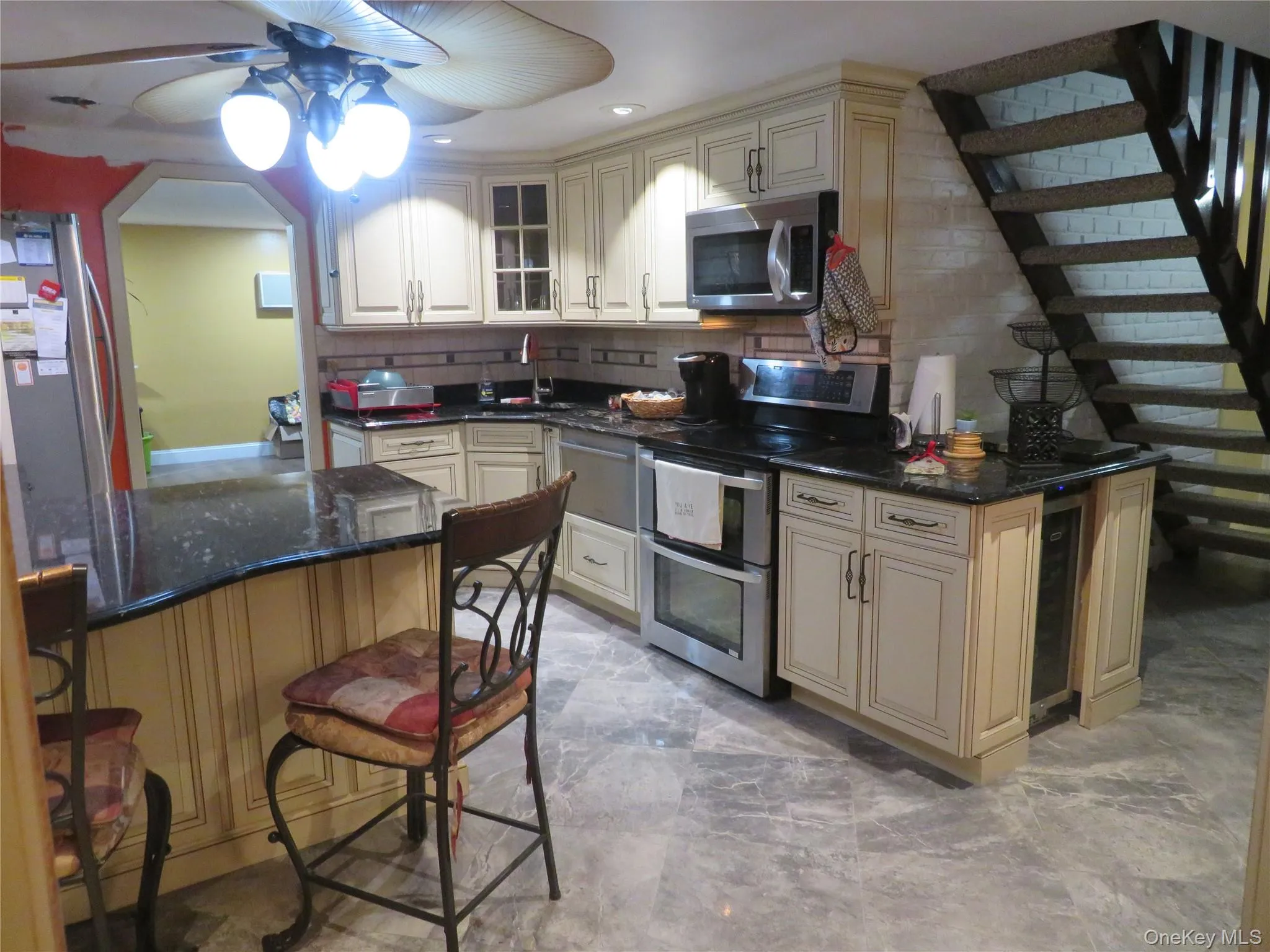 Kitchen featuring cream-toned cabinetry, dark stone countertops, stainless steel appliances, a built-in wine refrigerator, and stone-tile flooring Kitchen featuring cream-toned cabinetry, dark stone countertops, stainless steel appliances, a built-in wine refrigerator, and stone-tile flooring