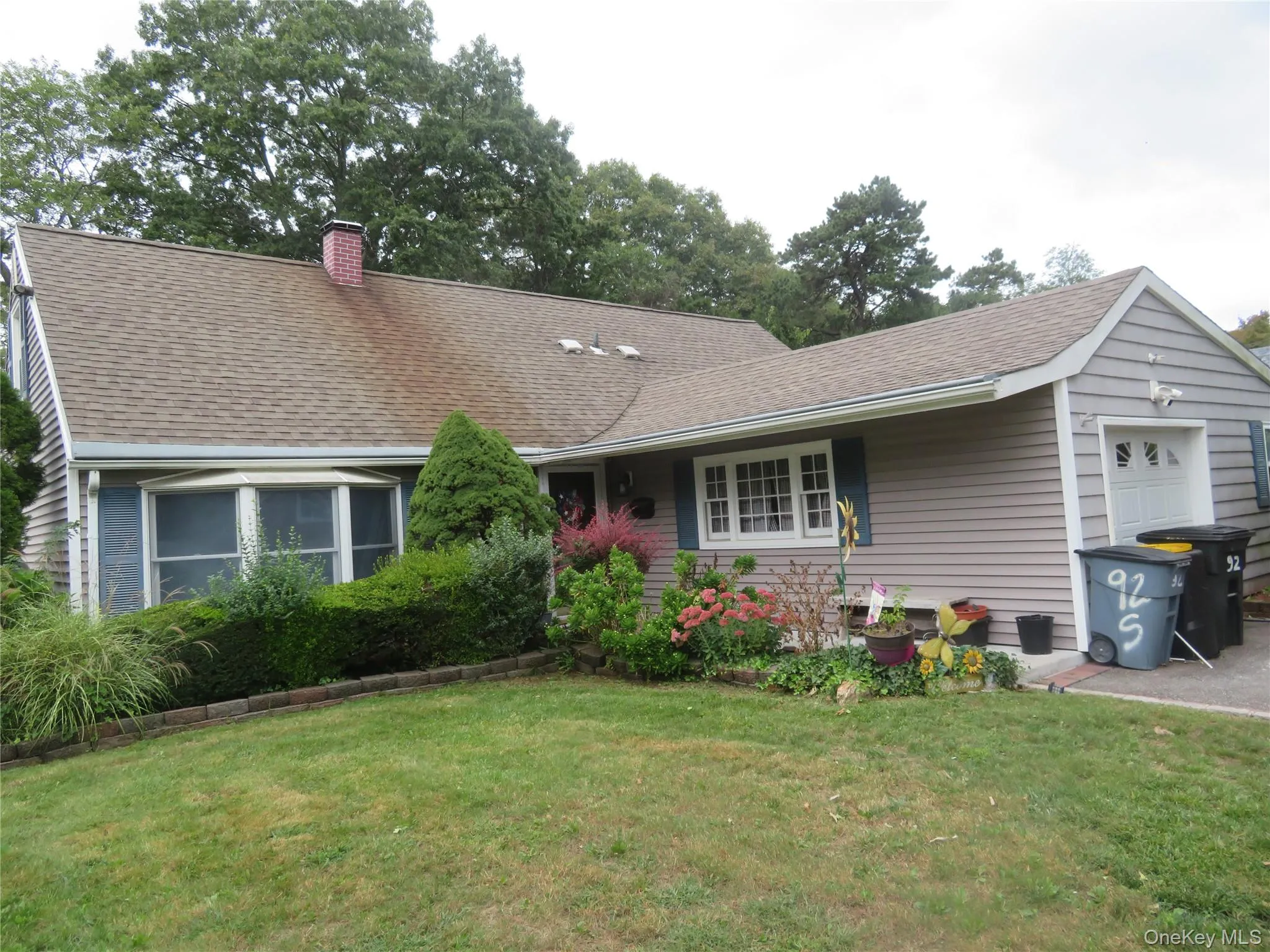 Front elevation featuring a brick chimney, bay window, attached garage, and manicured landscaping Front elevation featuring a brick chimney, bay window, attached garage, and manicured landscaping