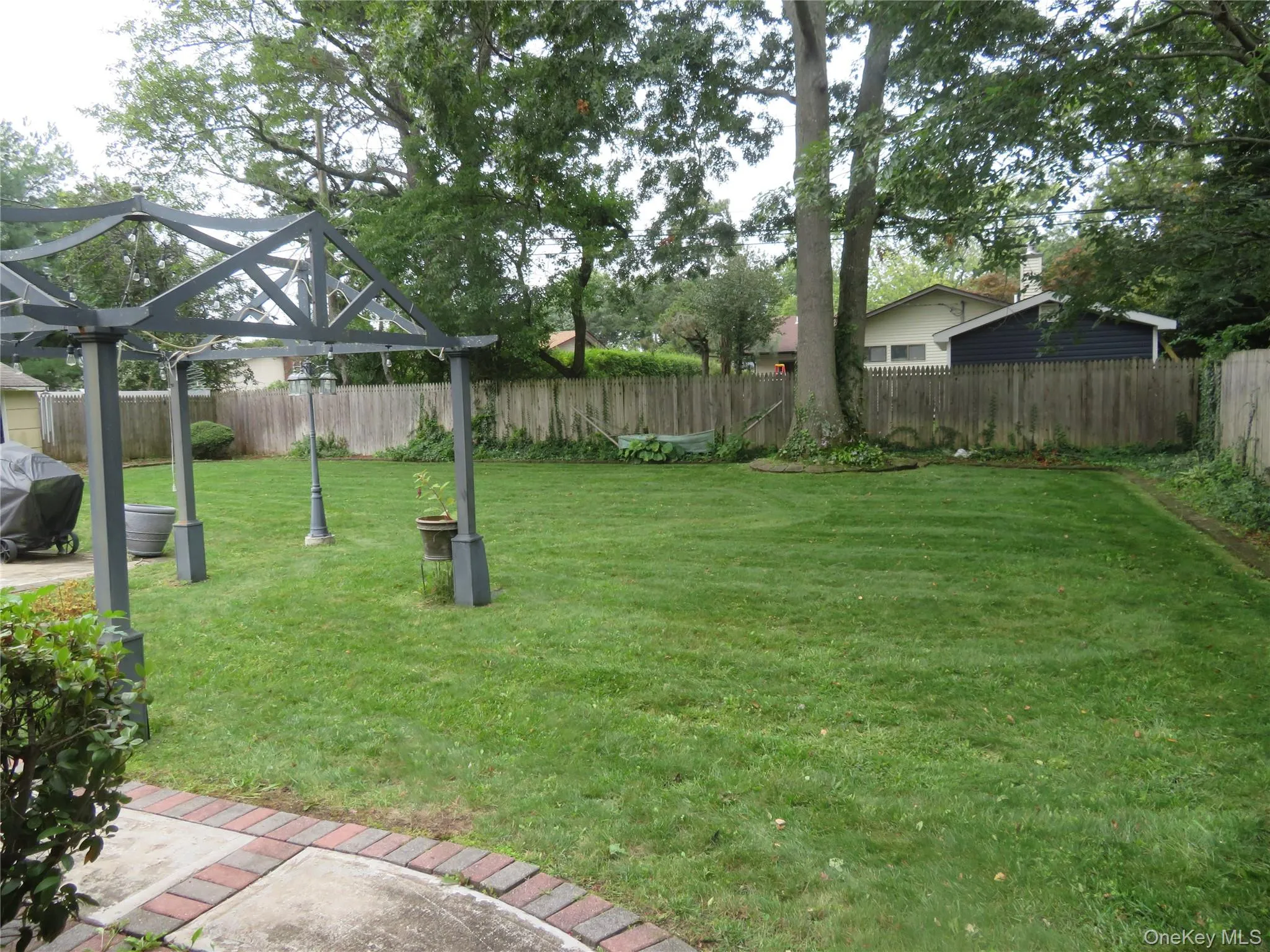 Expansive green lawn, mature trees, wood fence enclosure, and a decorative pergola structure Expansive green lawn, mature trees, wood fence enclosure, and a decorative pergola structure