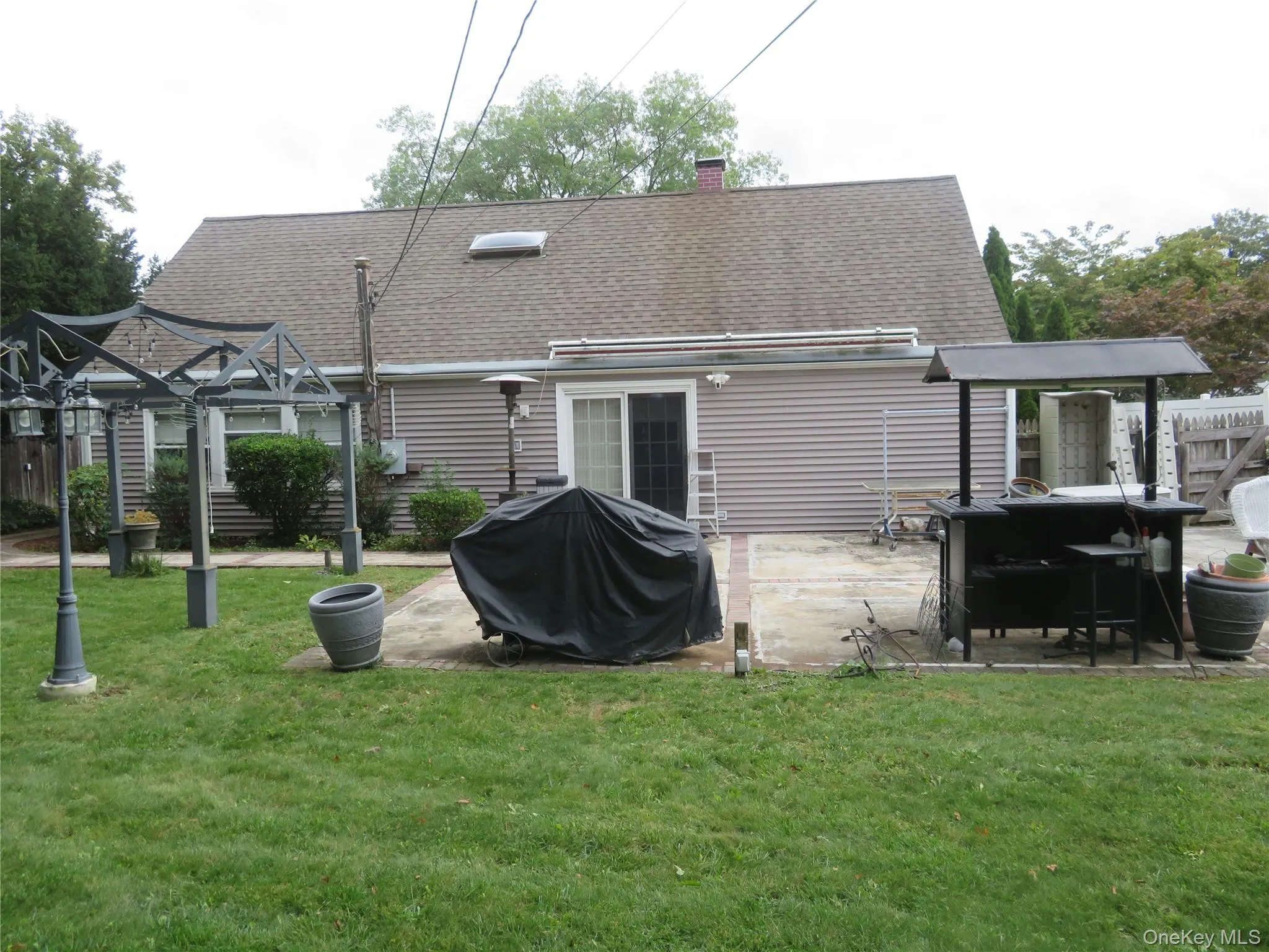 Expansive backyard with a concrete patio featuring a sliding glass door, a metal gazebo structure, and a secondary structure with a dark roof Expansive backyard with a concrete patio featuring a sliding glass door, a metal gazebo structure, and a secondary structure with a dark roof