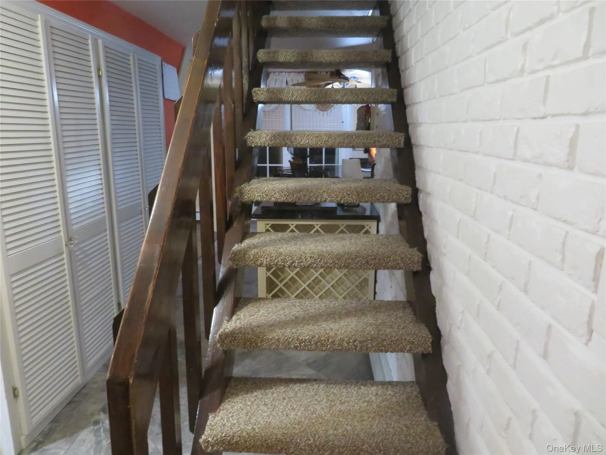 Open-tread staircase featuring dark wood structural supports, carpeted steps, and a painted white brick accent wall Open-tread staircase featuring dark wood structural supports, carpeted steps, and a painted white brick accent wall