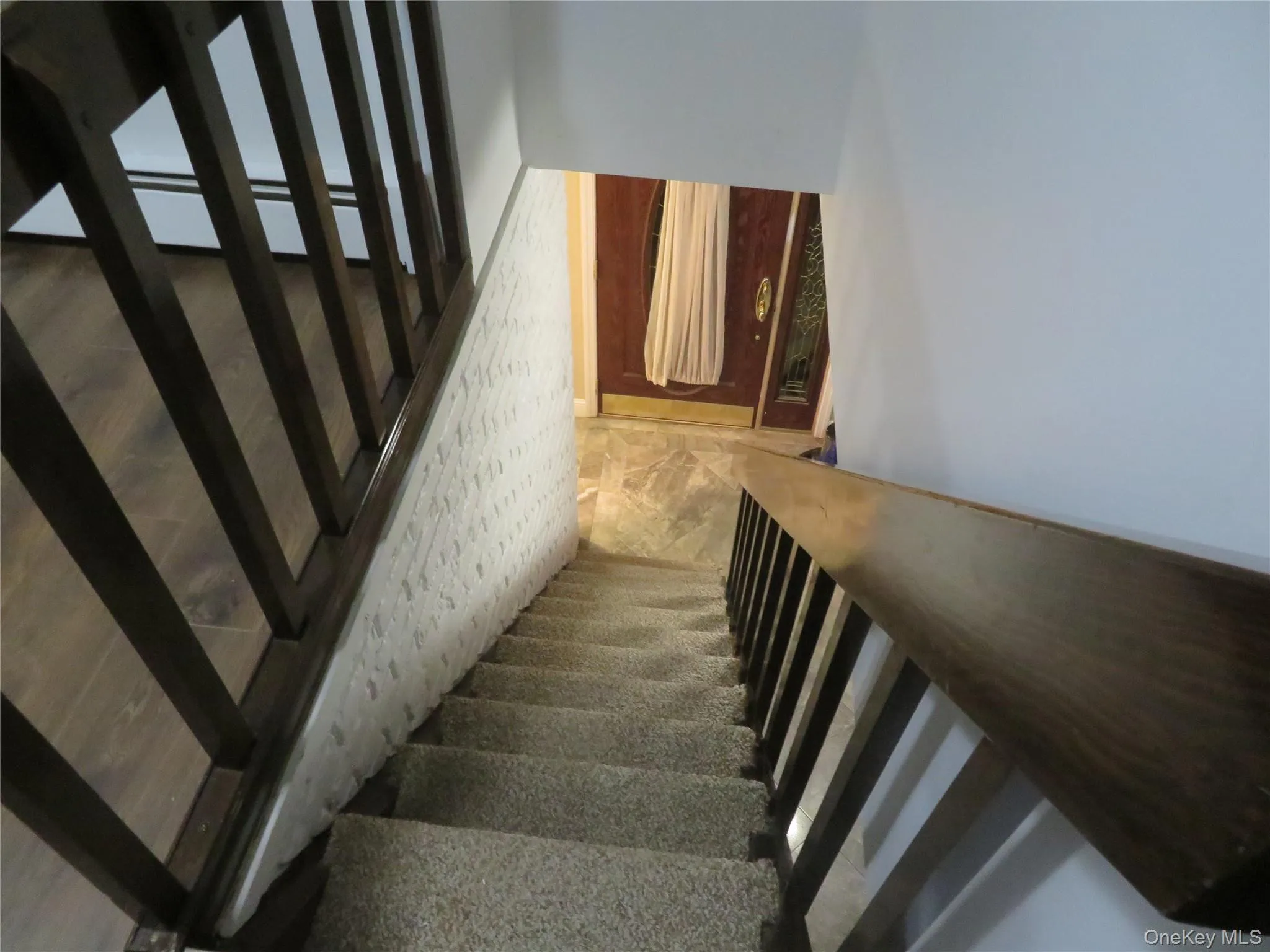 Staircase going Down featuring wood-finish railings, textured white wall detailing, and carpeted treads Staircase going Down featuring wood-finish railings, textured white wall detailing, and carpeted treads