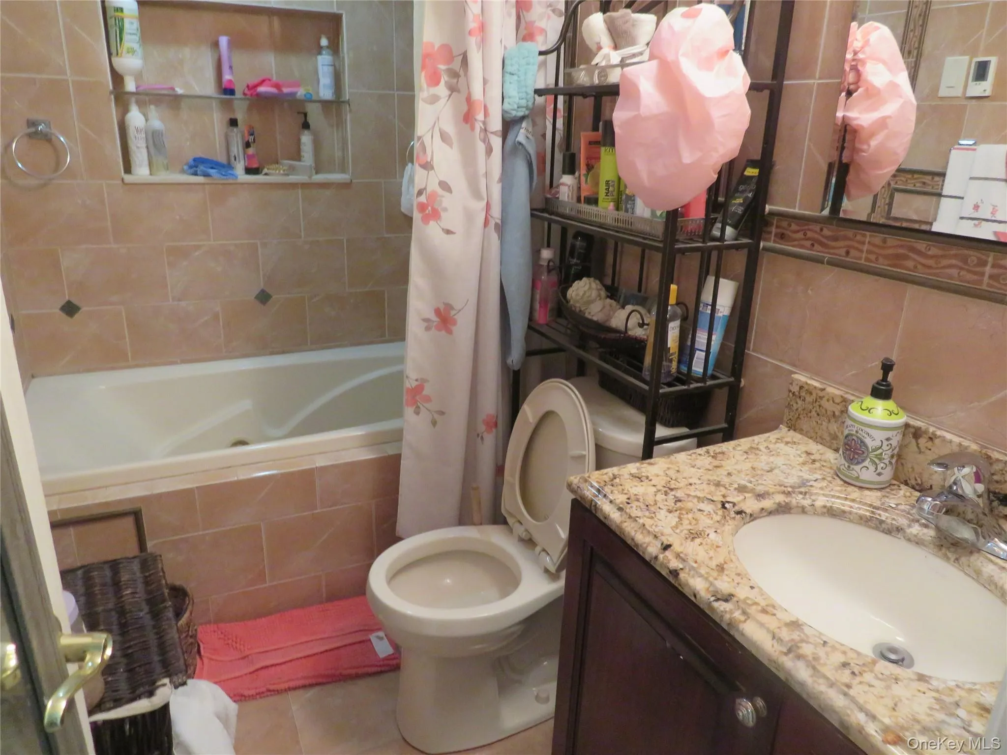Brown tiled bathroom featuring a built-in bathtub, a vanity with a granite countertop, and a built-in shelf Brown tiled bathroom featuring a built-in bathtub, a vanity with a granite countertop, and a built-in shelf