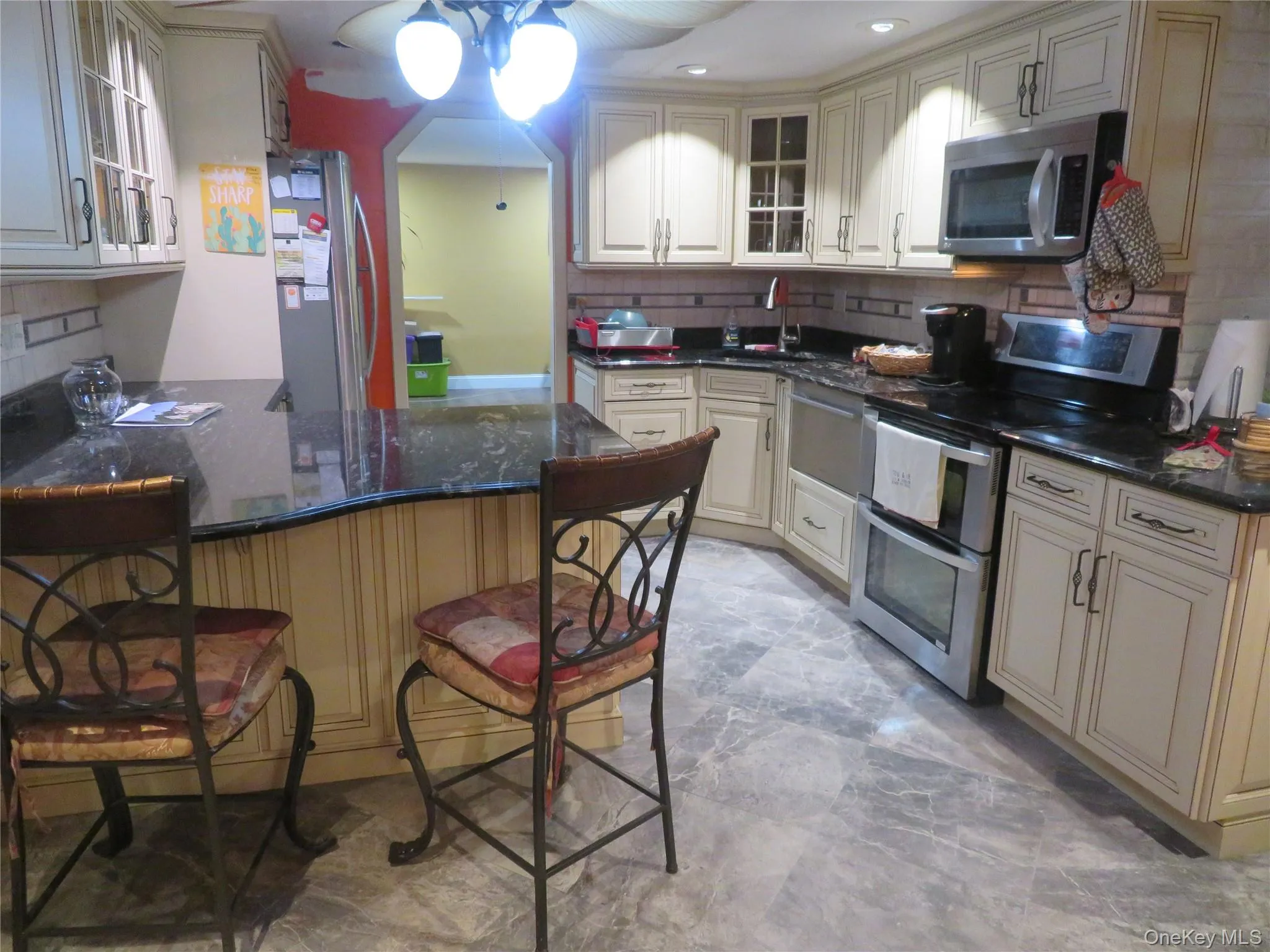 Kitchen featuring off-white cabinetry, dark stone countertops, stainless steel appliances, and stone-finish tile flooring Kitchen featuring off-white cabinetry, dark stone countertops, stainless steel appliances, and stone-finish tile flooring