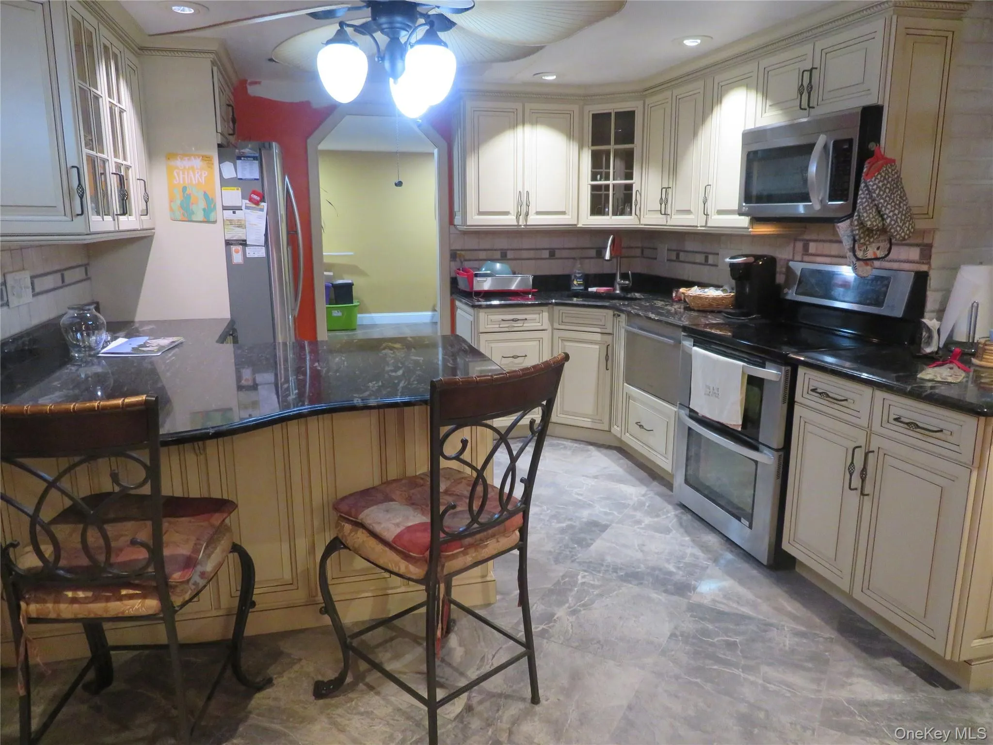 Kitchen featuring off-white cabinetry with crown molding, dark stone countertops, stainless steel appliances, and stone-tile flooring Kitchen featuring off-white cabinetry with crown molding, dark stone countertops, stainless steel appliances, and stone-tile flooring