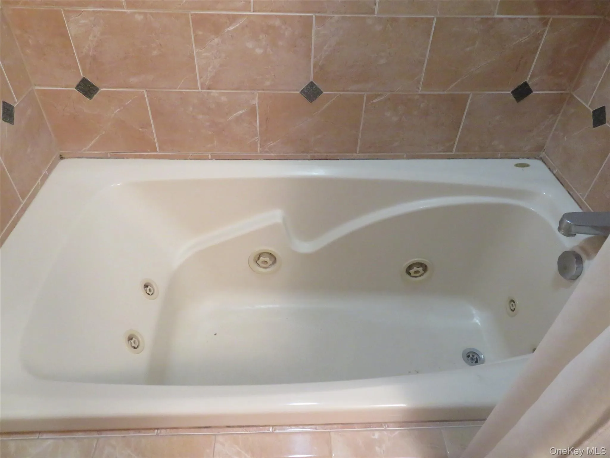 Built-in soaking tub with multiple jets, integrated bath faucet, and surrounding tile work with decorative accents Built-in soaking tub with multiple jets, integrated bath faucet, and surrounding tile work with decorative accents