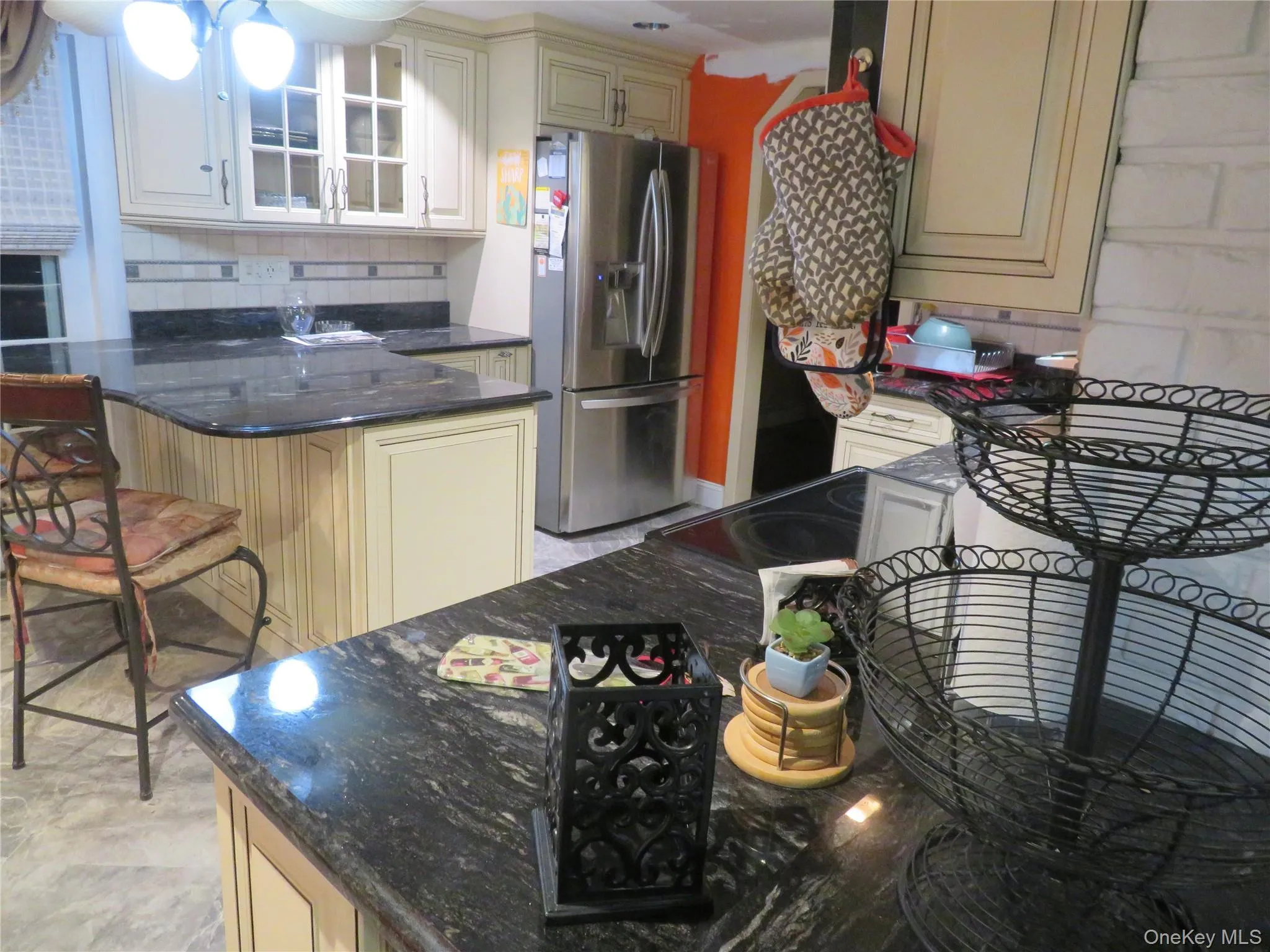 Kitchen featuring custom cabinetry with glass-front uppers, stone countertops, a multi-level island, stainless steel refrigerator, and built-in stovetop Kitchen featuring custom cabinetry with glass-front uppers, stone countertops, a multi-level island, stainless steel refrigerator, and built-in stovetop