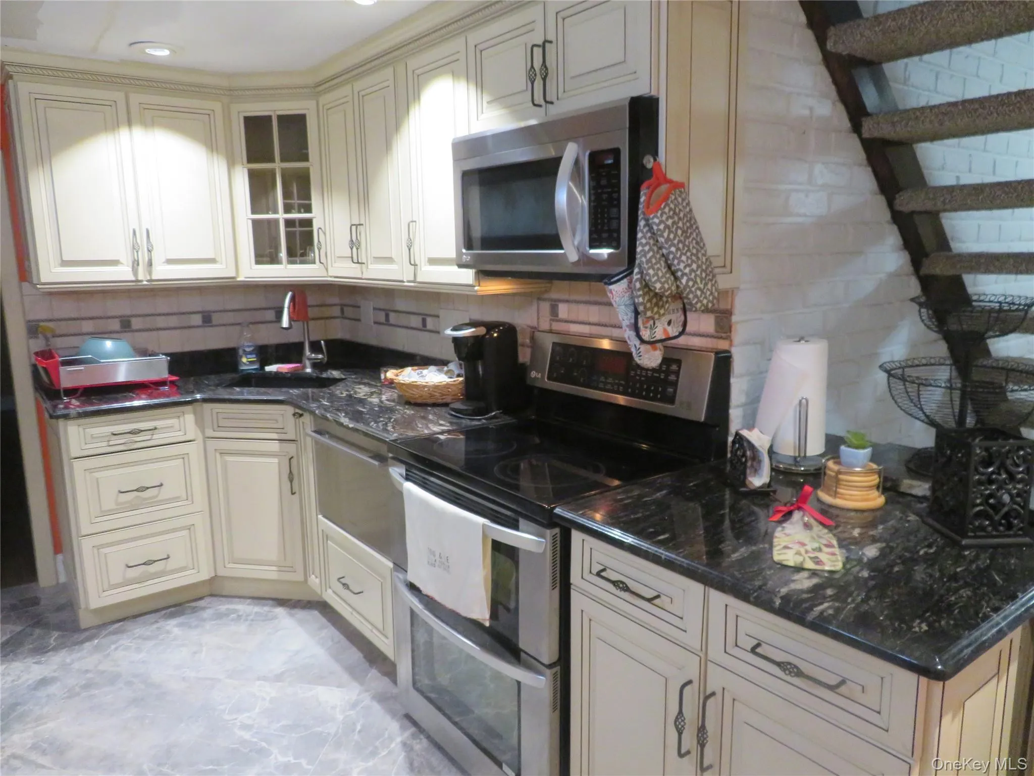 Kitchen featuring off-white cabinetry, dark stone countertops, stainless steel appliances, recessed ceiling lighting, and tile flooring Kitchen featuring off-white cabinetry, dark stone countertops, stainless steel appliances, recessed ceiling lighting, and tile flooring