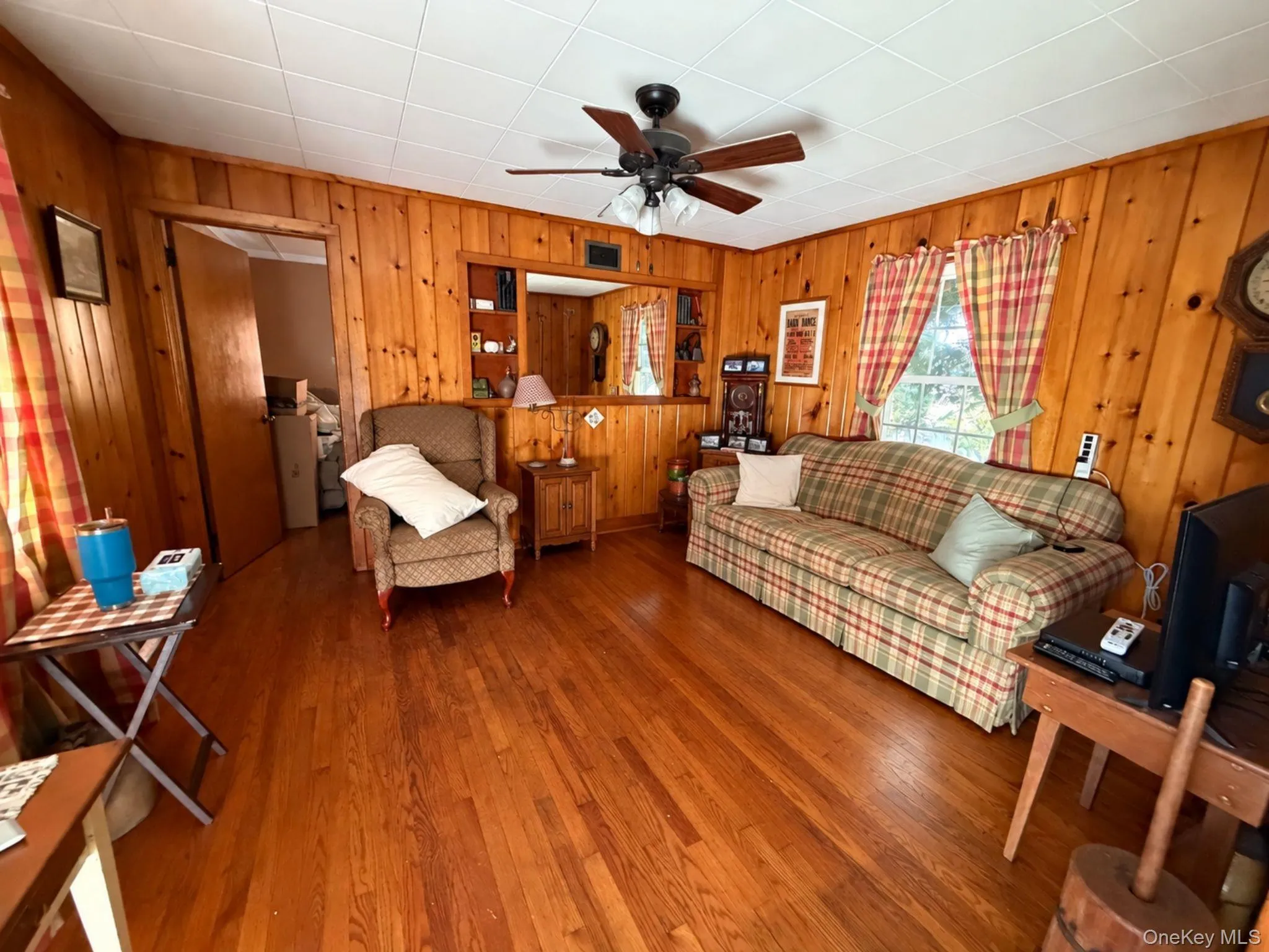 Hardwood flooring, wood paneling, ceiling fan, built-in shelving, and a window. Room virtually decluttered. Hardwood flooring, wood paneling, ceiling fan, built-in shelving, and a window. Room virtually decluttered.
