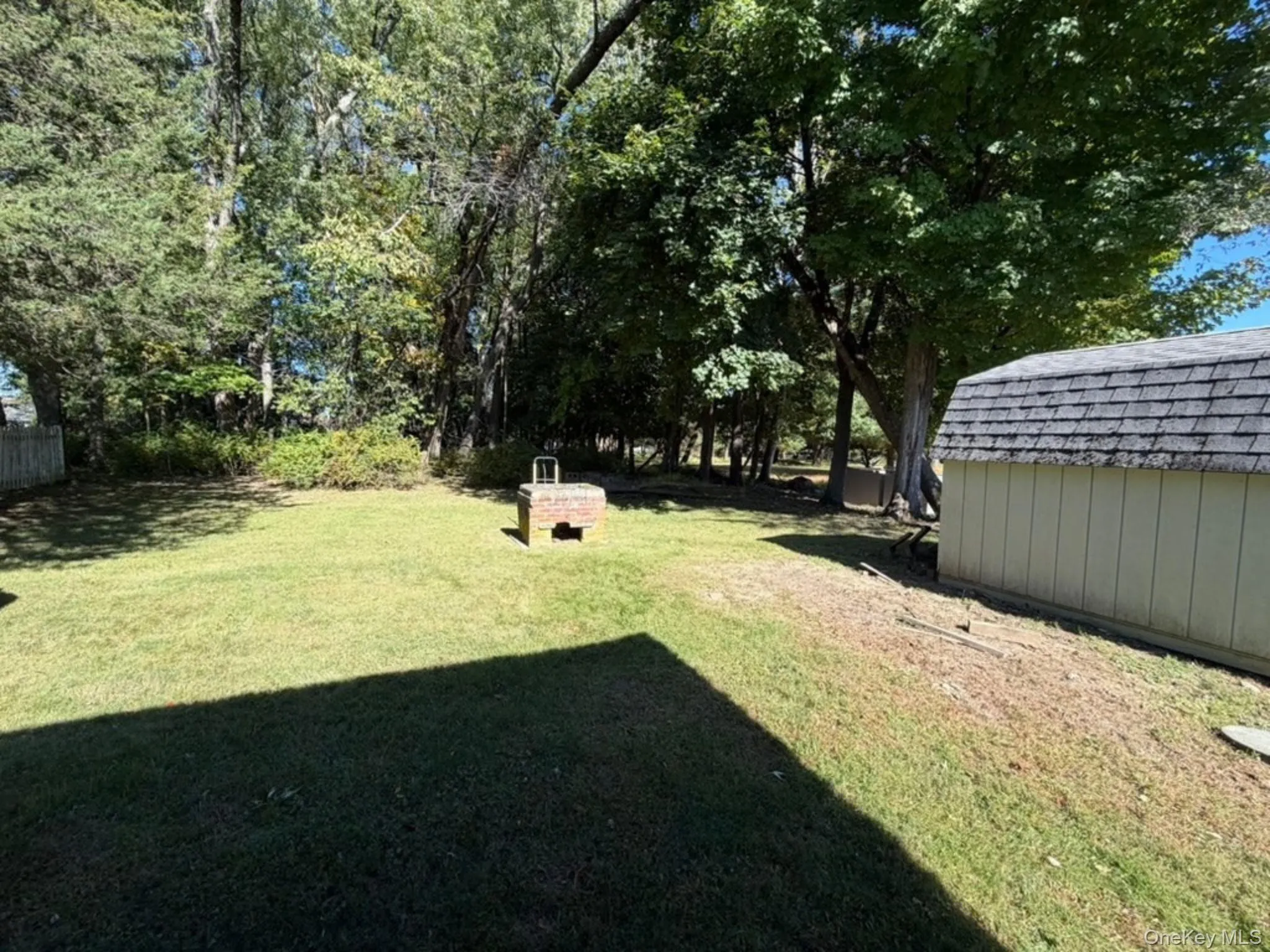 Expansive grassy yard with mature trees, a detached storage shed, and a brick-built fire pit Expansive grassy yard with mature trees, a detached storage shed, and a brick-built fire pit
