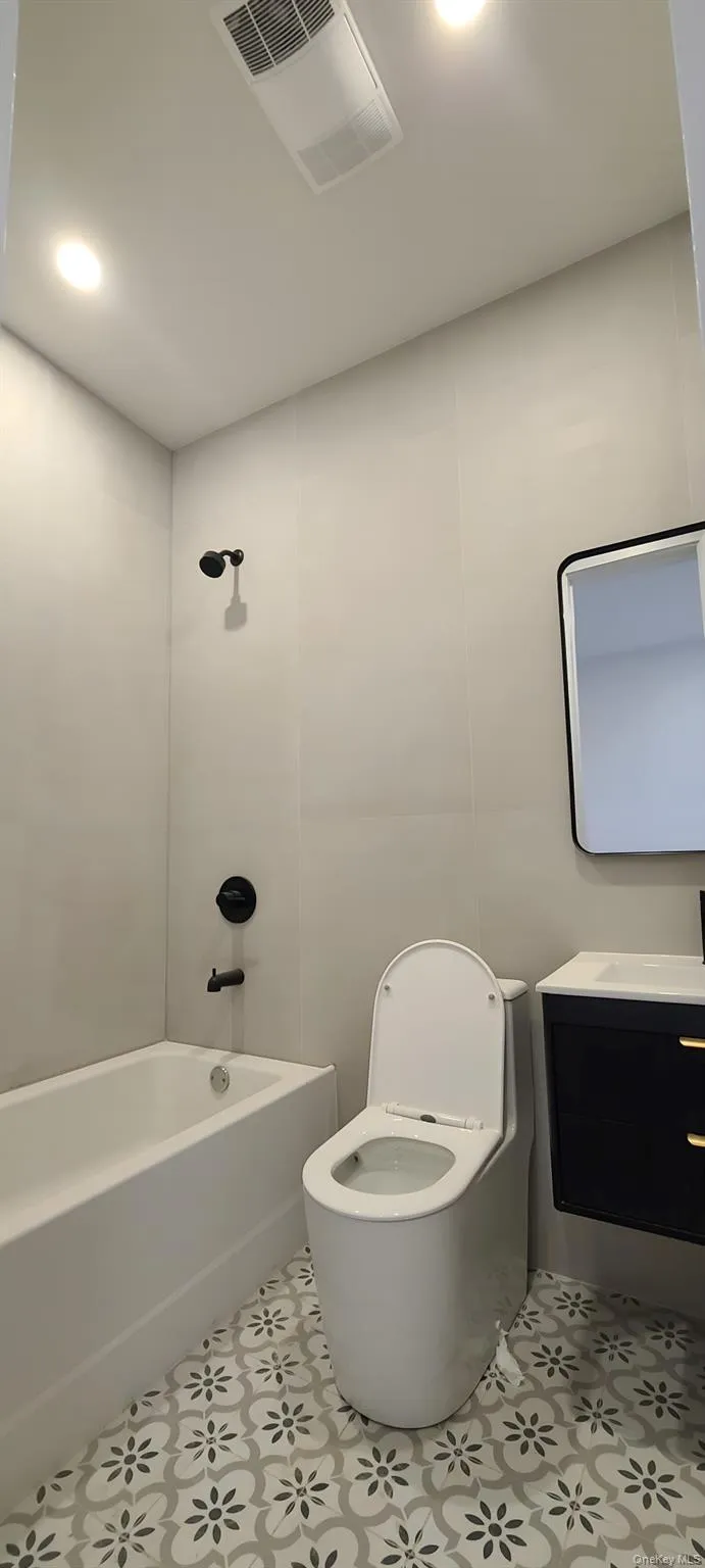 Bathroom featuring a white bathtub, black shower fixtures, a modern toilet, and patterned floor tiles Bathroom featuring a white bathtub, black shower fixtures, a modern toilet, and patterned floor tiles
