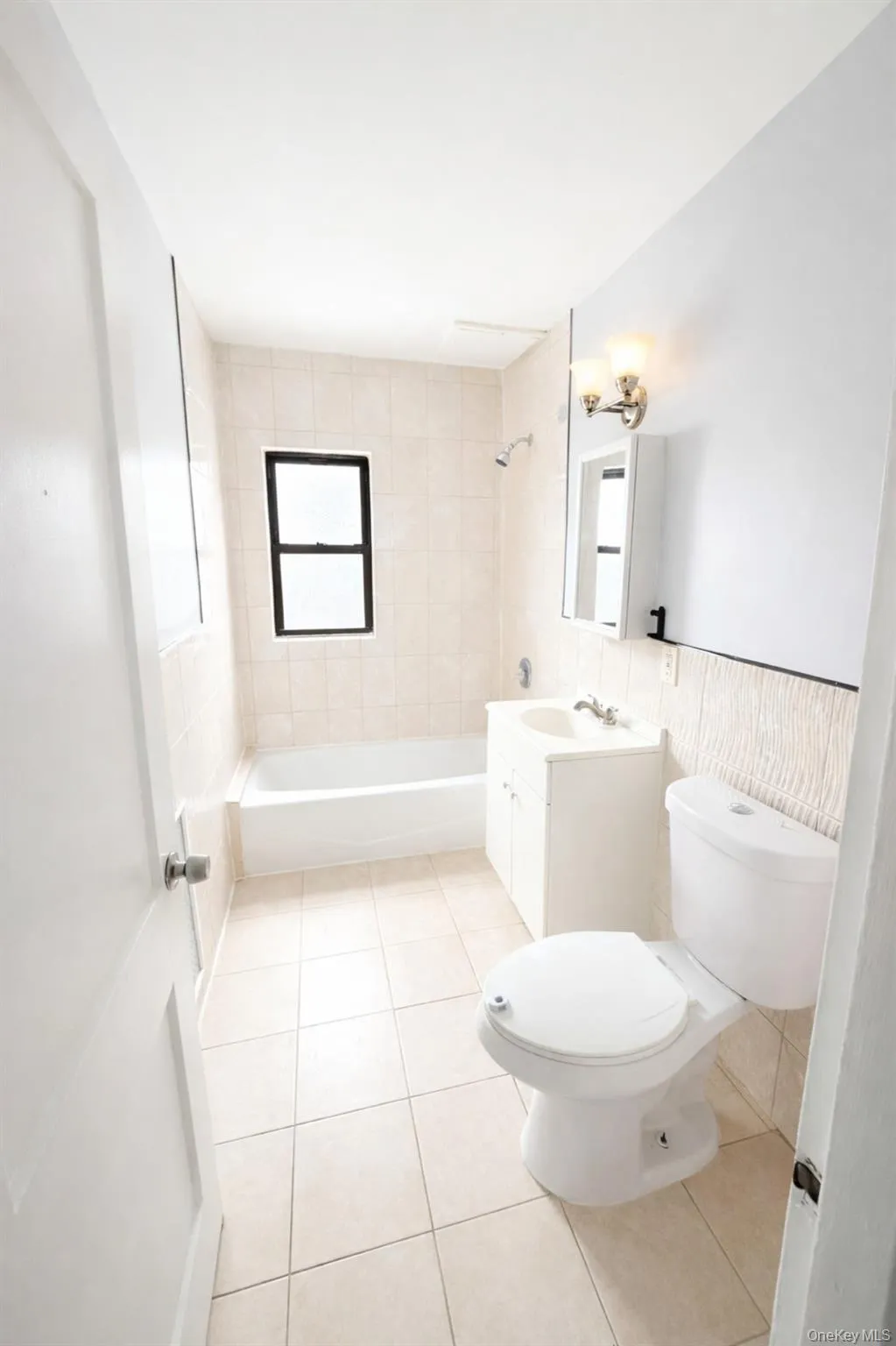 Full bath with vanity, tile walls, tub / shower combination, light tile patterned flooring, and wainscoting Full bath with vanity, tile walls, tub / shower combination, light tile patterned flooring, and wainscoting