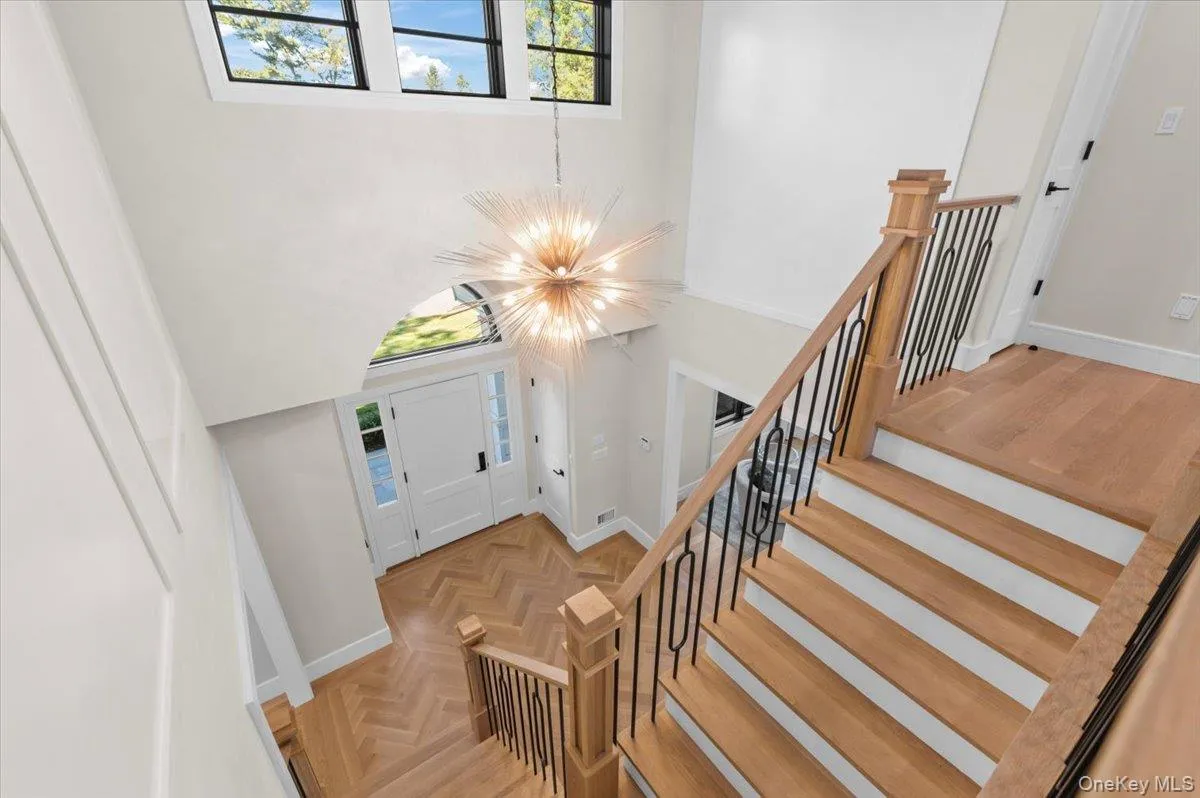Two-story entry foyer featuring a striking chandelier, herringbone wood-finish flooring, and a grand staircase with wrought iron balusters Two-story entry foyer featuring a striking chandelier, herringbone wood-finish flooring, and a grand staircase with wrought iron balusters