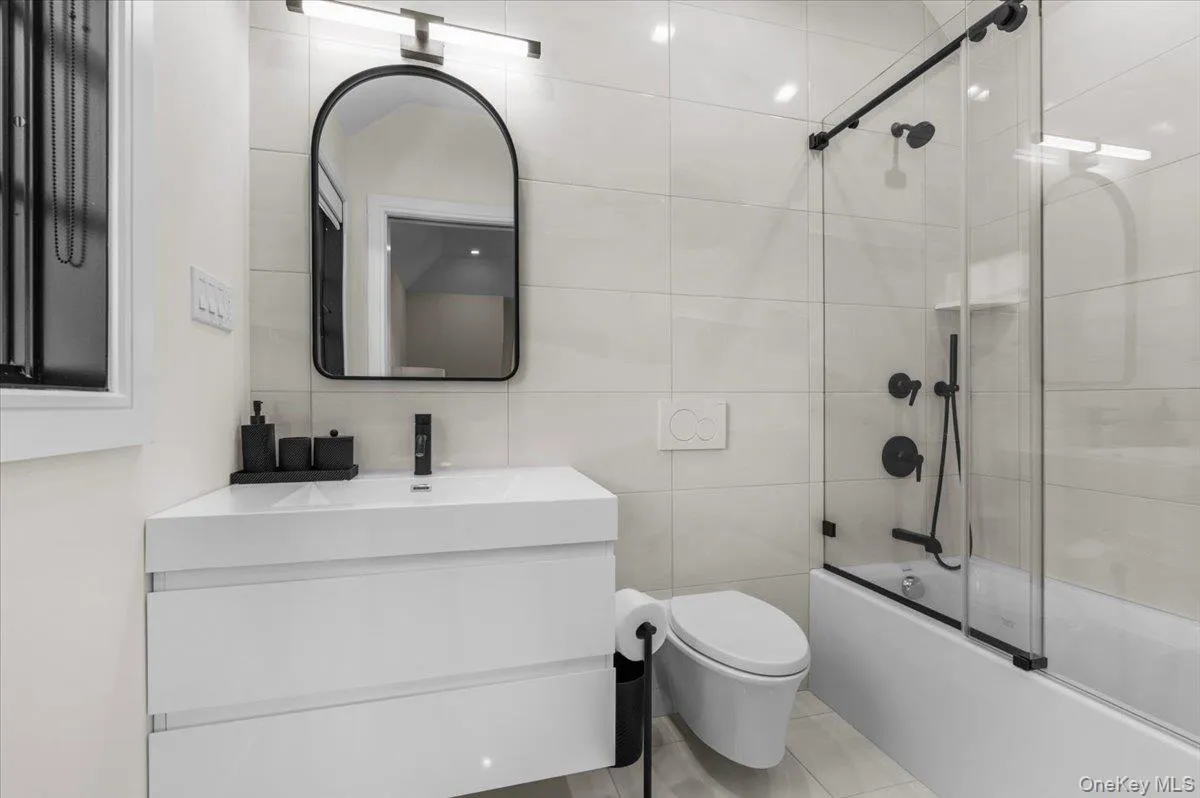 Floating vanity with integrated sink, black-framed arched mirror, black matte fixtures, and full-height wall tiling Floating vanity with integrated sink, black-framed arched mirror, black matte fixtures, and full-height wall tiling