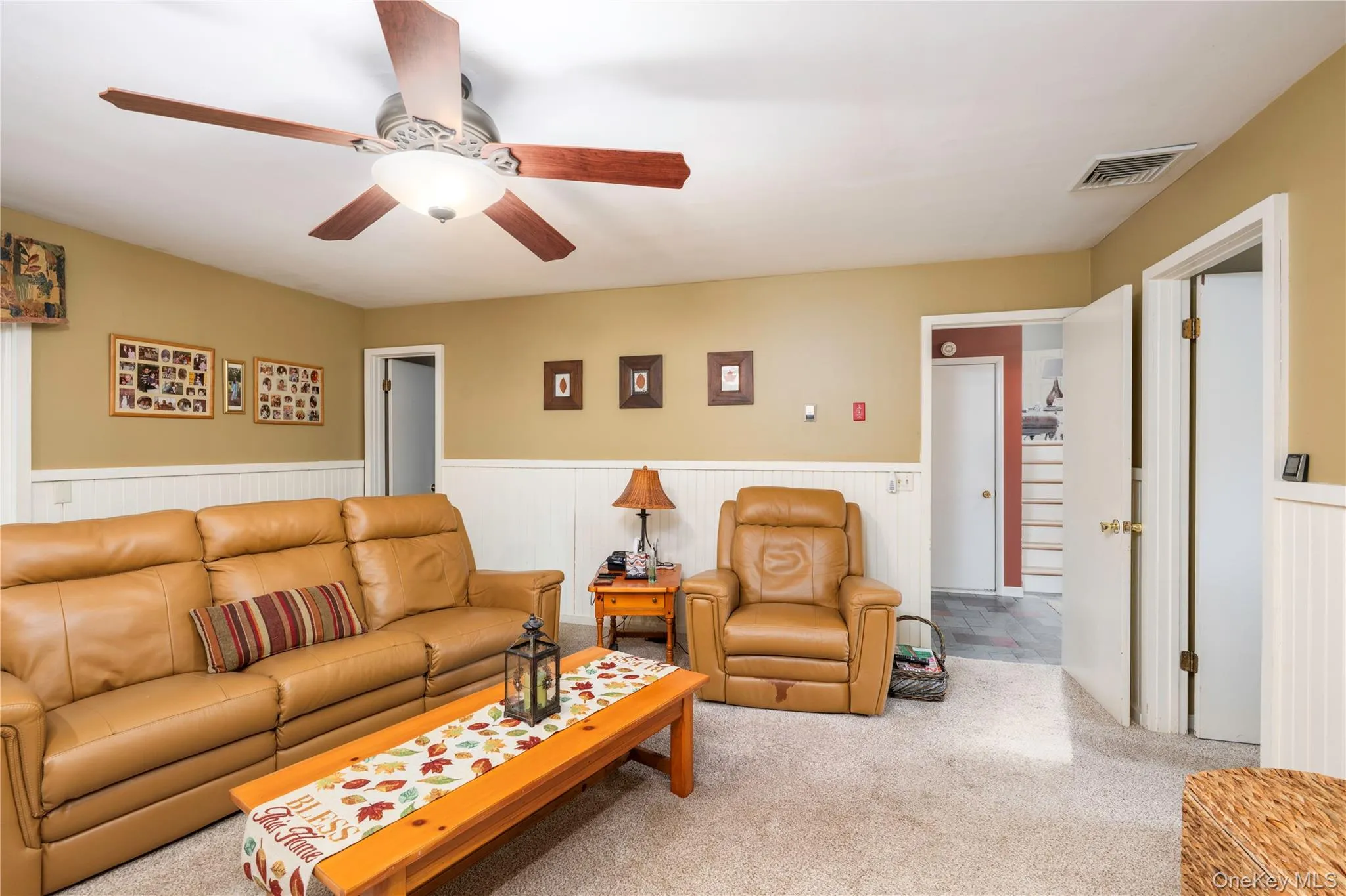 Interior space featuring wall-mounted wainscoting, carpeted flooring, and a ceiling-mounted light fixture with a fan Interior space featuring wall-mounted wainscoting, carpeted flooring, and a ceiling-mounted light fixture with a fan