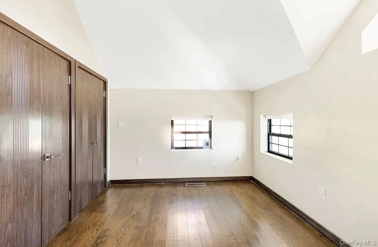 Hardwood flooring with dark baseboards, vaulted ceilings, two built-in closet units, and two windows with blinds Hardwood flooring with dark baseboards, vaulted ceilings, two built-in closet units, and two windows with blinds