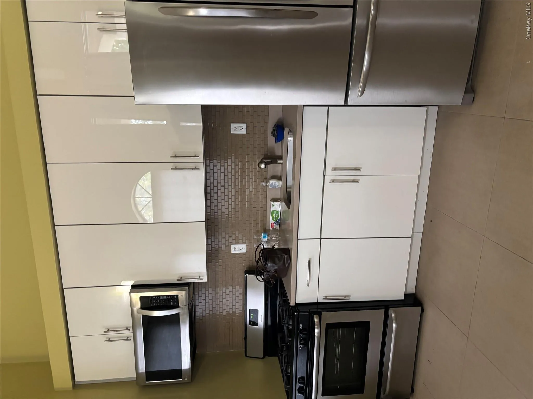 Kitchen featuring white cabinetry, stainless steel appliances, a tile backsplash, and light-toned flooring Kitchen featuring white cabinetry, stainless steel appliances, a tile backsplash, and light-toned flooring