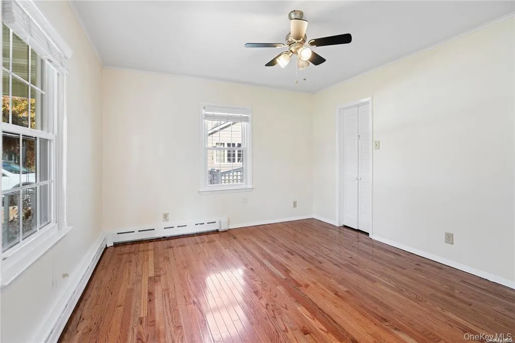 Bedroom featuring hardwood flooring, baseboard heating, a and a ceiling fan Bedroom featuring hardwood flooring, baseboard heating, a and a ceiling fan