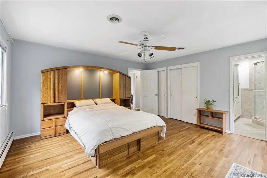 Bedroom featuring baseboard heating, light wood finished floors, multiple closets, and ceiling fan Bedroom featuring baseboard heating, light wood finished floors, multiple closets, and ceiling fan