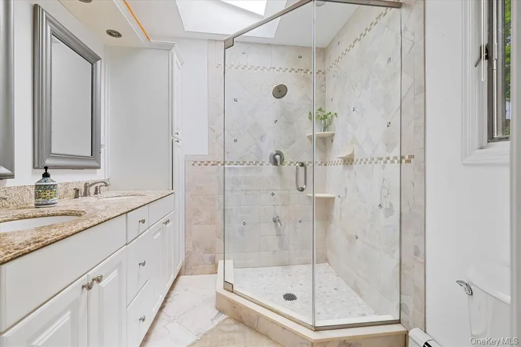 Full bathroom featuring a skylight, a stall shower, and double vanity Full bathroom featuring a skylight, a stall shower, and double vanity