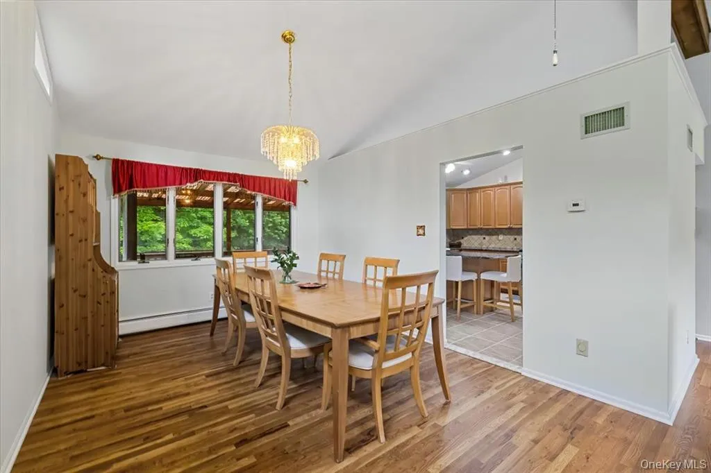 Dining area featuring light wood finished floors, lofted ceiling, a chandelier, and baseboard heating Dining area featuring light wood finished floors, lofted ceiling, a chandelier, and baseboard heating