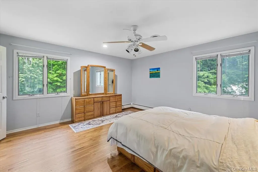 Bedroom with multiple windows, light wood finished floors, ceiling fan, and a baseboard heating unit Bedroom with multiple windows, light wood finished floors, ceiling fan, and a baseboard heating unit