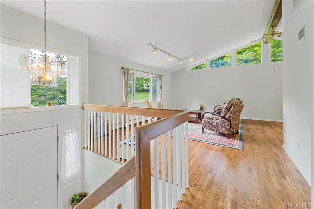Hall with an upstairs landing, rail lighting, wood finished floors, vaulted ceiling, and a chandelier Hall with an upstairs landing, rail lighting, wood finished floors, vaulted ceiling, and a chandelier