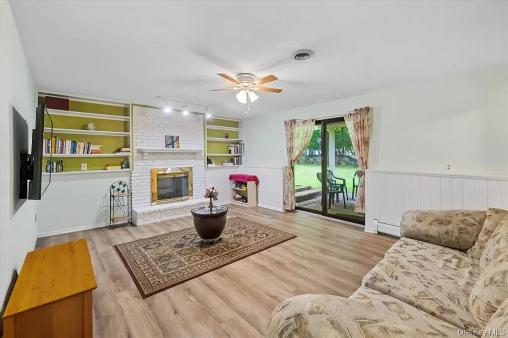 Living area featuring built in shelves, a fireplace, light wood-style flooring, a ceiling fan, and baseboard heating Living area featuring built in shelves, a fireplace, light wood-style flooring, a ceiling fan, and baseboard heating