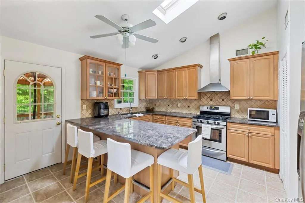 Kitchen with lofted ceiling, decorative backsplash, gas stove, a kitchen bar, and wall chimney range hood Kitchen with lofted ceiling, decorative backsplash, gas stove, a kitchen bar, and wall chimney range hood